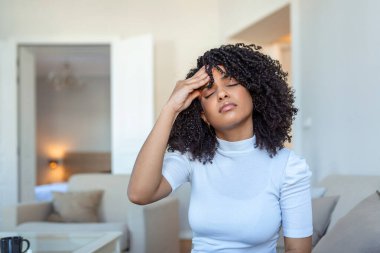 Çekici bir kadının portresi evde bir kanepede oturuyor, baş ağrısı çekiyor, acı çekiyor ve kendini kötü hissediyor. Üzgün kadın kanepeye uzanmış, şiddetli baş ağrısı çekiyor..