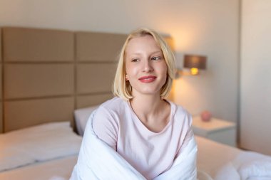Uyandıktan sonra battaniyeye sarılmış bir kadın, iyi bir uykudan sonra bir güne mutlu ve rahat giriyor. Tatlı rüyalar, günaydın, yeni gün, hafta sonu, tatil konsepti