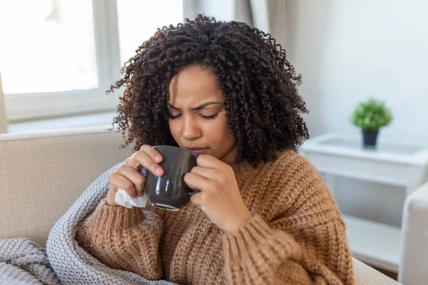 Sick young woman sitting at home in bed with hot cup of tea and handkerchief. Seasonal colds, cough, runny nose, viral infections, home treatment