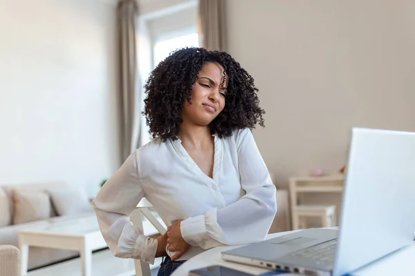 Back Pain Bad Posture Woman Sitting In Office. Young afro woman suffering from back pain while working on laptop at home