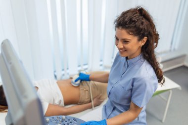 Karın bölgesinde ultrason taraması, klinikte kadın kadına, yakın çekim. Doktor hastanın karnına ultrason sensörü yerleştiriyor ve ekrandaki görüntüye bakıyor. İç organların teşhisi.