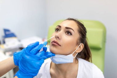 Maske takan kadın hasta, kokpit 19 testi için burundan örnek alıyor. Koruyucu ekipmanlı bir sağlık çalışanı kadına koronavirüs örneği veriyor. Covid-19 için burun çubuğu.