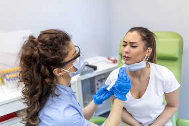 Kadın hasta, eldivenler ve PPE giysisiyle korunan bir sağlık uzmanı tarafından burun çubuğuyla Covid-19 testi yaptırıyor. Coronavirüs salgını sırasında hızlı antijen testi.
