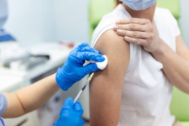 Klinikte kadın aşılayan bir pratisyen. Hastanede kadına iğne yapan bir doktor. Hemşire elinde şırınga ve iğne Covid-19 ya da koronavirüs aşısı. Enjeksiyon kovid aşı konsepti..