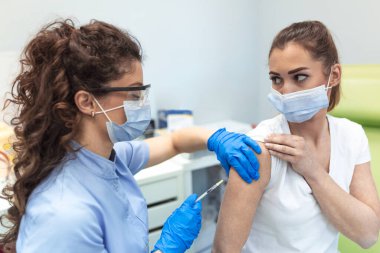 Klinikte kadın aşılayan bir pratisyen. Hastanede kadına iğne yapan bir doktor. Hemşire elinde şırınga ve iğne Covid-19 ya da koronavirüs aşısı. Enjeksiyon kovid aşı konsepti..