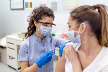 Hastanedeki pratisyen hekim hastaya fotokopi alanı aşıladı. Doktor kadına iğne yapıyor. Covid-19 ya da Coronavirus aşısı yapmadan önce şırınga tutan ve pamuk kullanan hemşire..