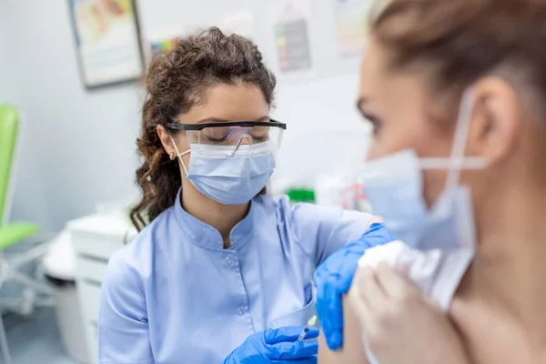 医師はマスクを身に着けている女性患者の肩の中にCovid 19ワクチン注射用量を作る注射器を保持 インフルエンザワクチン臨床試験の概念コロナウイルス治療クローズアップ — ストック写真