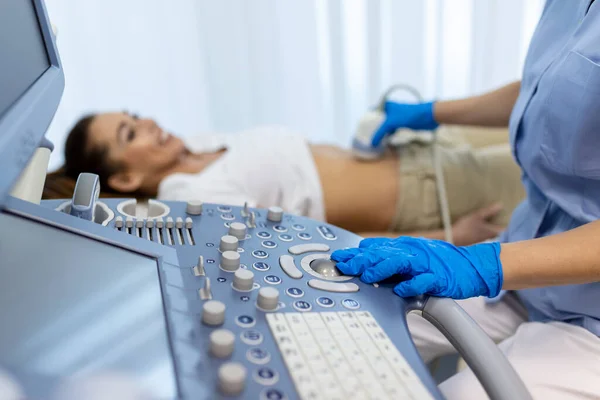 在检查女病人时 用超声波扫描仪对穿着白色实验室外套和无菌手套的妇科医生进行侧视画像 女人躺在床上 背影朦胧 — 图库照片