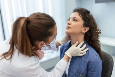 İlaç, sağlık ve sağlık muayenesi konsepti - hastanede hastanın bademciklerini kontrol eden doktor ya da hemşire. Endokrinolog klinikte genç bir kadının boğazını inceliyor.