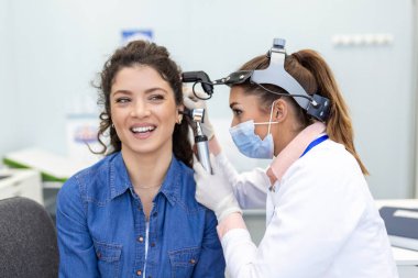 İşitme. Otolaryngologist doktor, klinikte otoskop ya da auriskop kullanarak kadının kulağını kontrol ediyor. Otorhinolarbilimadamı elleriyle kulağı çekiyor ve ona otoskopla yakından bakıyor..