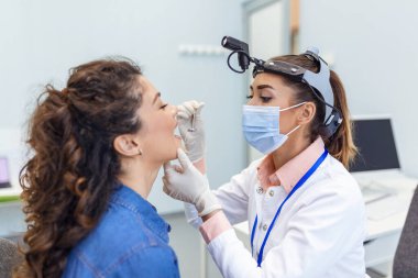 Genç bir kadın doktorunun karşısındaki muayene masasında oturuyor. Kadın kafasını kaldırıp dilini dışarı çıkarırken doktor bir dil bastırıcı ile öne uzanıyor..