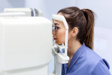 Modern klinikte özel optik cihazlarla gözleri test eden bir doktor. Oftalmolojist, göz hekimliği ofisinde yapılan tıbbi muayene sırasında dijital mikroskop kullanan bir hastanın gözlerini inceliyor.