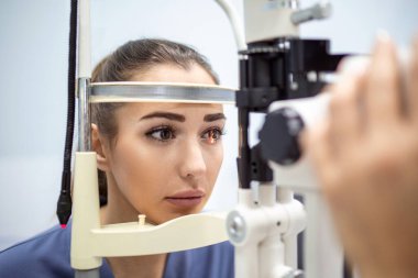 Optometrist, göz hekimliği kliniğindeki yarık lamba üzerinde kadın hastayı muayene ediyor. Genç ve güzel bir kadına özel göz tansiyonu teşhisi konur..