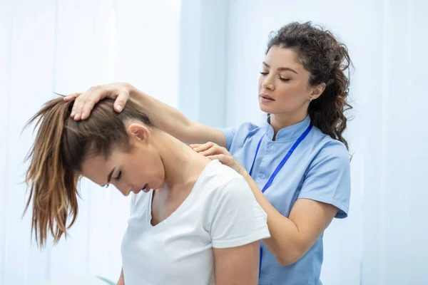 Licensed chiropractor or manual therapist doing neck stretch massage to relaxed female patient in clinic office. Young woman with whiplash or rheumatological problem getting professional doctor's help