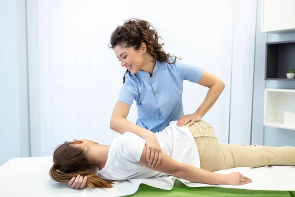 Young woman doctor chiropractor or osteopath fixing lying womans back with hands movements during visit in manual therapy clinic. Professional chiropractor during work