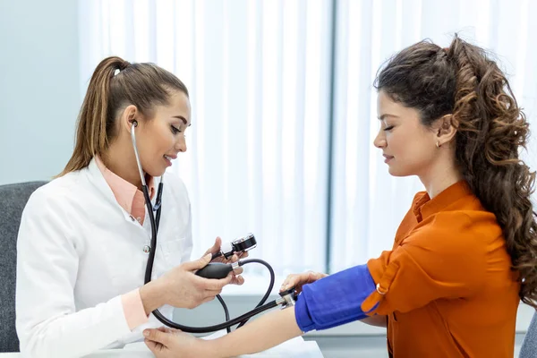 血圧の測定 若い女性は現代の診療所で女性医師と面会している 血圧の測定 圧力計 高血圧と高心拍数 — ストック写真