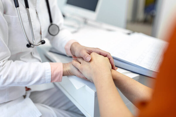 Young female doctor hold hand of caucasian woman patient give comfort, express health care sympathy, medical help trust support encourage reassure infertile patient at medical visit, closeup view.