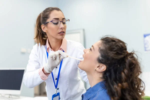 stock image Female patient opening her mouth for the doctor to look in her throat. Female doctor examining sore throat of patient in clinic. Otolaryngologist examines sore throat of patient.