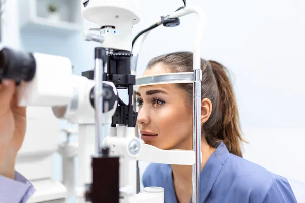 眼科诊所在缝隙灯检查女病人的注意验光师 在特殊的眼科设备上诊断出年轻漂亮的女人有眼压 — 图库照片