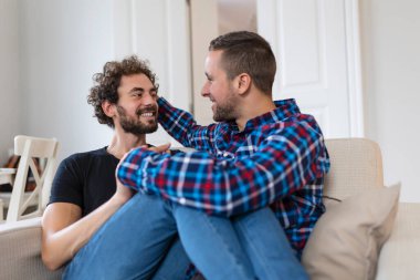 Neşeli genç eşcinsel çift birlikte oturuyor. İki sevecen erkek aşık birbirlerini kucaklarken neşeyle gülümsüyorlar. Genç gay coupe romantik oluyor..