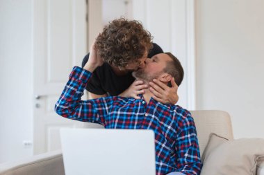 Evlerinde otururken öpüşen sevimli eşcinsel çift. İki romantik genç erkek aşık içeride internette sörf yaparken eğleniyor. Genç eşcinsel çift birlikte yaşıyor..