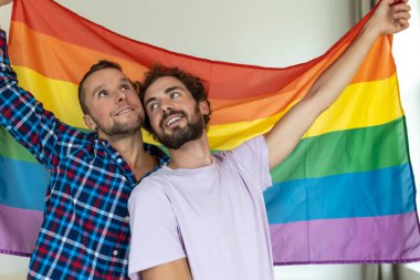 İki genç eşcinsel aşık birbirine sevgiyle bakıyor. Gurur bayrağına karşı birlikte duran iki genç erkek aşık. Sevecen genç eşcinsel çift romantik bir anı paylaşıyor..