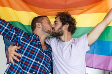 İki genç eşcinsel sevgili birbirlerini sevgiyle öpüyorlar. Gurur bayrağına karşı birlikte duran iki genç erkek aşık. Sevecen genç eşcinsel çift romantik bir anı paylaşıyor..