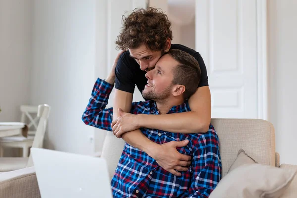 stock image Lovely gay couple laughing together while sitting in their living room at home. Two romantic young male lovers having fun surfing the internet indoors. Young gay couple living together.