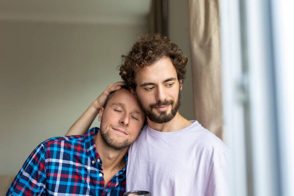 Cheerful young gay couple sitting together. Two affectionate male lovers smiling cheerfully while embracing each other. Young gay coupe being romantic.