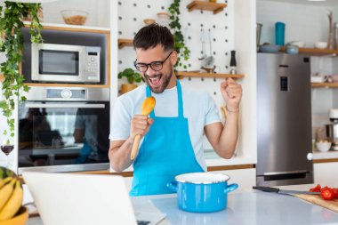 Çekici genç adam mutfakta dans ediyor ve şarkı söylüyor..