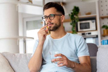 Genç adam doktorunun yazdığı ilaçları alıyor. Hap alıp bir bardak su içen bir adam. Sağlık, ilaç, tedavi kavramı