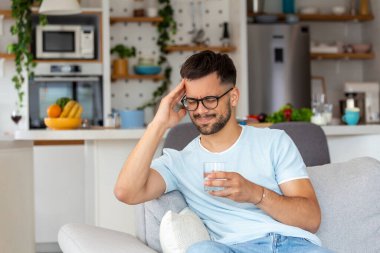 Evdeki kanepede su içerken başı ağrıyan depresyonlu genç bir adam..
