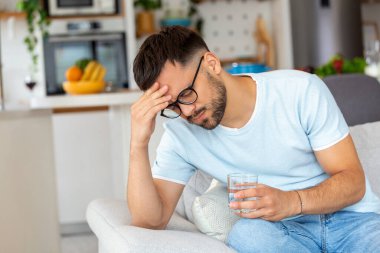 Evdeki kanepede su içerken başı ağrıyan depresyonlu genç bir adam..