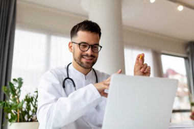Erkek doktorun portresi dizüstü bilgisayarlı ekranda hastayla konuşuyor klinik masasında oturmuş yerel sağlık tedavisi için online danışmanlık yapıyor. Uzaktan kumandalı sağlık randevusu
