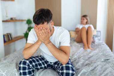 Kız arkadaşıyla tartıştıktan sonra üzgün düşünceli bir adam. İlişki sorunları, çatışma ve aile kavramı, yatak odasında sorunları olan mutsuz bir çift. Üzgün adam yatakta oturuyor, kız arkadaşı arka planda.