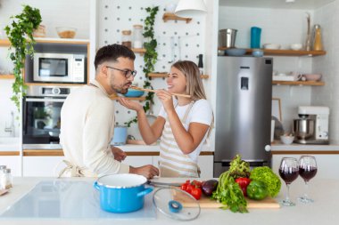 Güzel genç çift birbirlerini besliyor ve evde yemek pişirirken gülümsüyor. Mutlu çift hafif mutfakta sağlıklı yiyecekler hazırlıyor. Sağlıklı gıda konsepti.