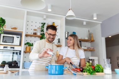 Mutfakta birlikte yemek pişiren, birlikte harika vakit geçiren gülümseyen genç bir çift. Erkek ve kadın gülüyor