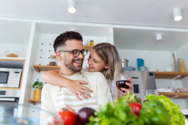 Romantik genç çift mutfakta birlikte yemek pişiriyor, birlikte harika vakit geçiriyorlar. Erkek ve kadın gülüyor ve şarap içiyor.