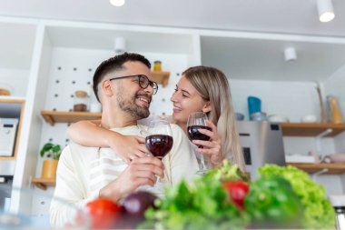 Güzel genç çift her birine bakıyor ve evde yemek pişirirken şarap içiyor. Sevgi dolu genç bir çift. Sarılmak ve yemek yapmak. Mutfakta eğlenmek.