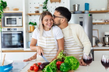 Evdeki mutfakta birlikte yemek pişiren mutlu genç çiftin portresi. Romantik genç kadın ve yakışıklı erkek aydınlık modern mutfakta dururken birlikte vakit geçirmekten zevk alıyorlar..