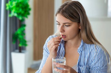 Korkunç acıdan acı çekme kavramı. Güzel, üzgün, üzgün, mutsuz, sorunlu, sıradan kıyafetler giyen zayıf kadın bir kanepede oturup hap alıyor.