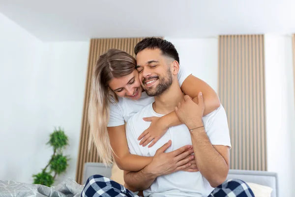 Portrait of young couple sitting on bed and look at each other. Attractive beautiful new marriage man and woman in pajamas enjoy morning activity in bedroom at home. Family relationship concept.