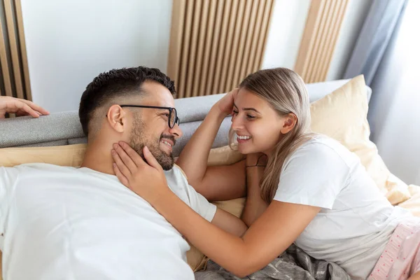 Portrait of young couple sitting on bed and look at each other. Attractive beautiful new marriage man and woman in pajamas enjoy morning activity in bedroom at home. Family relationship concept.
