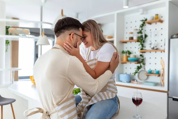 Affectionate young man kissing his wife while she's making breakfast. Beautiful young couple is talking and smiling while cooking healthy food in kitchen at home.Man is kissing his girlfriend in cheek