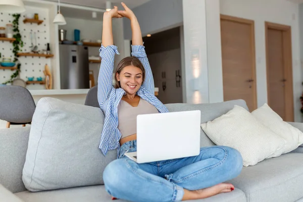 Image of satisfied young woman stretching arms, finish working on laptop. Woman sitting with computer on sofa, studying at home, e-learning and remote freelance job concept