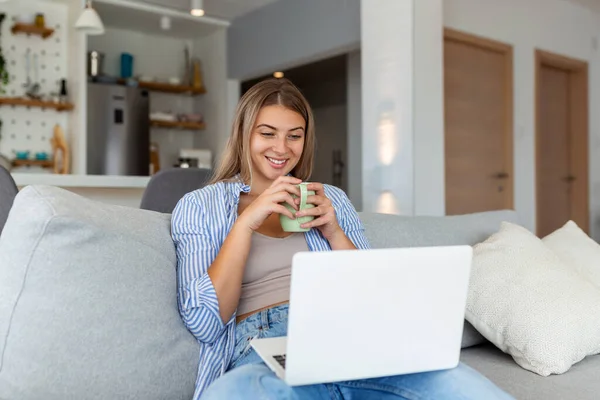 Positive young woman freelancer watching video in blog on netbook and having a coffee at comfortable home. Beautiful young business woman working on laptop.Freelancer connecting to internet