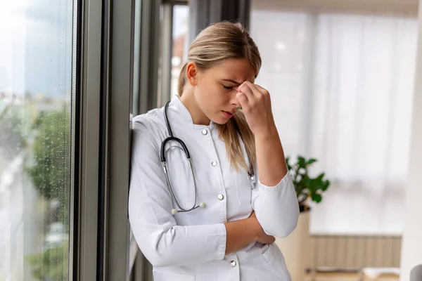 Young doctor looking distressed. Tired exhausted female doctor in uniform at hospital holding her head. Depressed sad doctor feels burnout stress