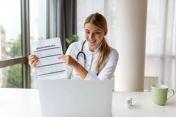 Stock image Attractive female doctor talking while explaining health insurance to patient through a video call with laptop in the consultation.