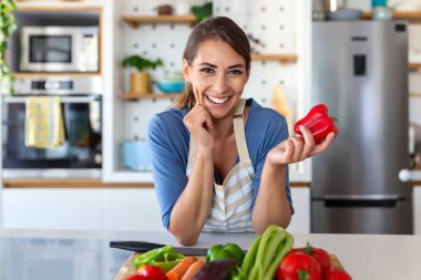 Cute happy young brunette woman in good mood preparing a fresh vegan salad for a healthy life in the kitchen of her home. clipart