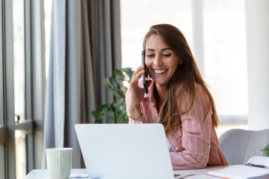 Ofisteki genç ve güzel iş kadını ofis koltuğunda oturmuş, akıllı telefonuyla konuşuyor.